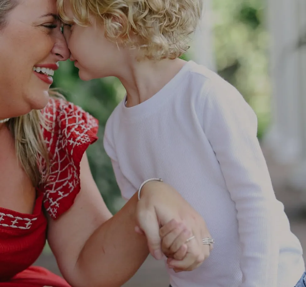 A mother and her young son laughing forehead to forehead on a porch