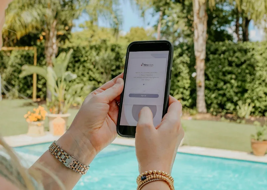 An agency owner opening the Sittysites app on her phone by a backyard pool